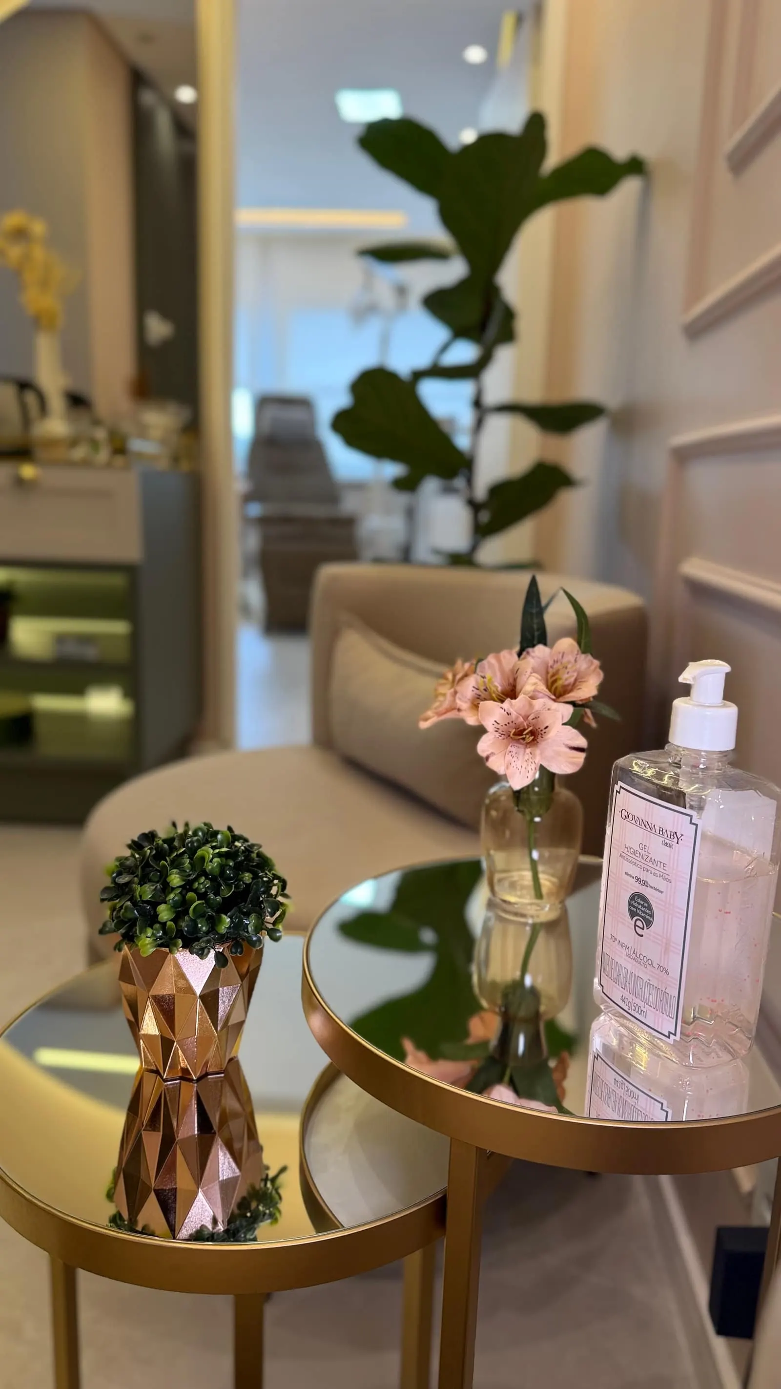 Sala de espera com mesas laterais douradas, plantas e arranjo de flores